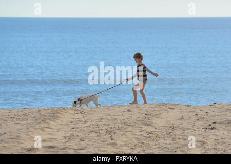 Junge mit Hund an der Leine, Bournemouth Beach, Dorset, Großbritannien, an einem warmen Oktobertag. Stockfoto