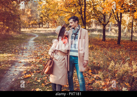 Junges Paar in Liebe Spaziergänge im Herbst Wald unter bunten Bäumen. Mann und Frau umarmen und sprechen bei Sonnenuntergang Stockfoto