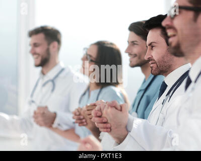 Ärzte sitzen in einer Reihe und halten die Hände voneinander Stockfoto