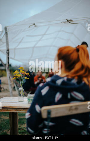 Blumenstrauß am Tisch der open-air Bar in Leipzig, Deutschland, mit rothaarigen Frau im Vordergrund. Stockfoto
