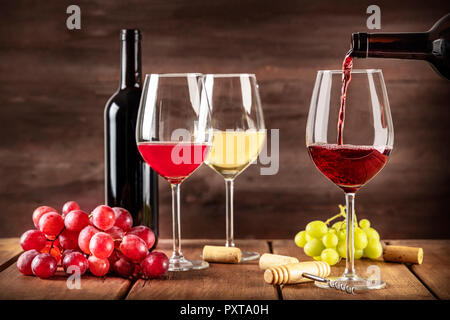 Die Weinprobe. Rotwein in ein Glas gegossen aus einer Flasche mit Kopie Raum und andere Gläser und Trauben in den unscharfen dunklen rustikalen Hintergrund Stockfoto