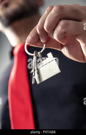 Haus-förmige Schlüsselbund mit Schlüssel holded durch einen eleganten Mann mit roter Krawatte. Die vertikale Ausrichtung der Foto. Stockfoto