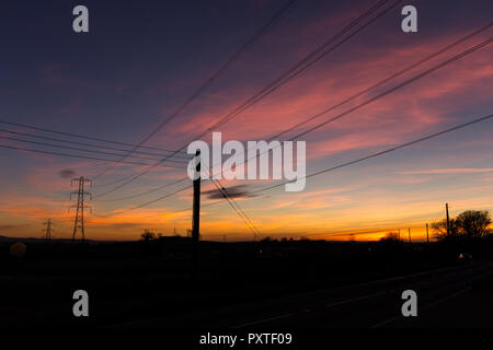 Farbenfroher Sonnenuntergang mit Strommasten und Leitungen gegen den Himmel. Carr, County Down, Nordirland. Stockfoto