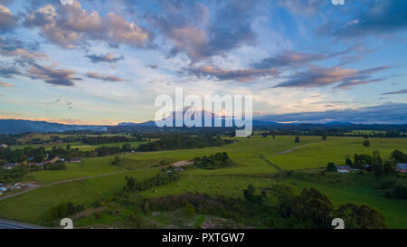 Felder von Gras und grünen Wald, mit dem calbuco Vulkan und Wolken im Hintergrund am Nachmittag Stockfoto