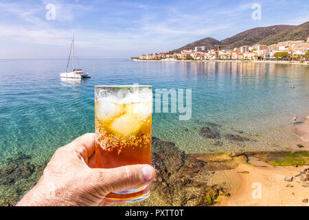 Hand mit einem Rum und Cola Cocktail in Glas mit Eis, St Francoise Strand, Ajaccio, Korsika Stockfoto