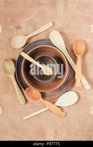 Home Küche Dekor: die Keramik Teller und Löffel aus Holz auf Holz- Hintergrund. Im rustikalen Stil. Blick von oben. Stockfoto