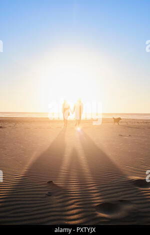 Portugal, Algarve, Paar mit Hund zu Fuß am Strand bei Sonnenuntergang Stockfoto