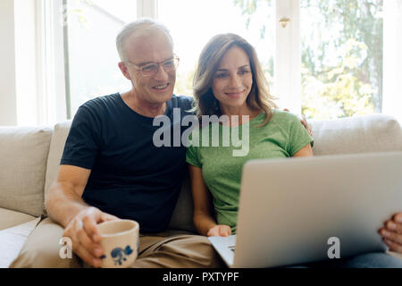 Lächelnd reifes Paar sitzt auf der Couch zu Hause teilen Laptop Stockfoto