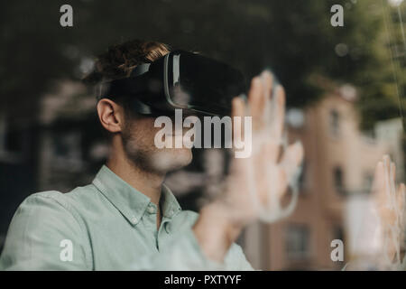 Junge Mann am Fenster mithilfe von VR-Brille Stockfoto