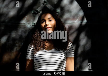 Junge Frau lehnte sich gegen alte Tür mit Baum Schatten Stockfoto