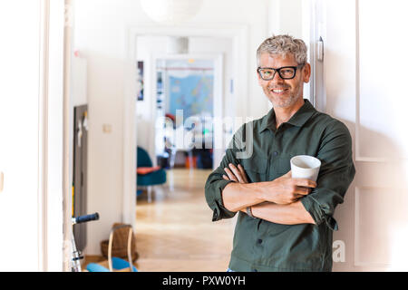 Portrait von lächelnden reifer Mann mit Kaffee Cup gegen Tür Fall zu Hause Schiefe Stockfoto