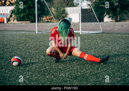 Junge Frau, die sich auf Fußball Boden neben dem Ball Stockfoto