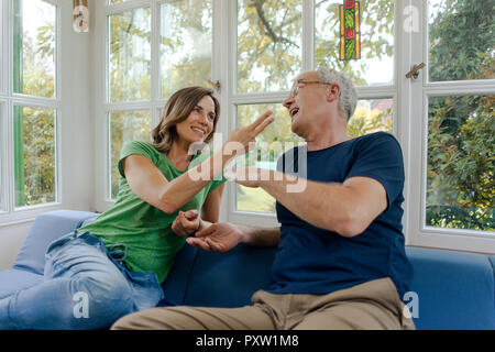 Gerne reifes Paar sitzt auf der Couch zu Hause spielt, Schere Papier Stein Stockfoto