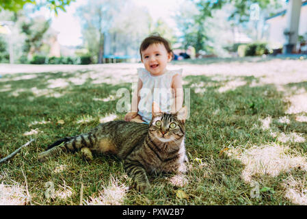 Portrait von tabby Cat auf einer Wiese mit lachendes Baby Mädchen im Hintergrund sitzen Stockfoto