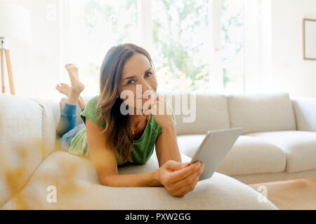 Portrait von lächelnden reife Frau liegen auf der Couch zu Hause mit der Tablette Stockfoto