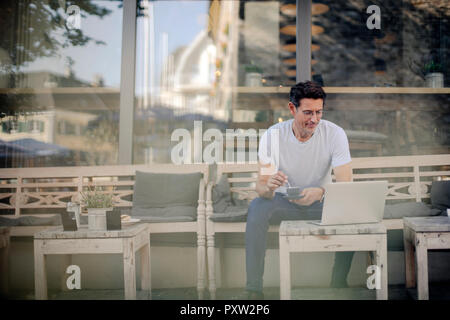 Unternehmer im Café sitzen, Kaffee trinken, mit Laptop Stockfoto