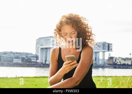 Deutschland, Köln, rothaarige junge Frau mit Handy Stockfoto