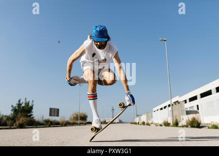 Mann in stilvollen sportlichen Outfit stehen auf Skateboard gegen den blauen Himmel Stockfoto