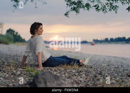 Frau sitzt am Fluss, Sonnenuntergang beobachten Stockfoto
