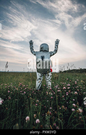 Spaceman erkunden Natur, stehend in der Wiese, winken Stockfoto