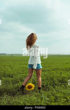 Junge Frau zu Fuß Holding eine Sonnenblume in ein grünes Feld Stockfoto