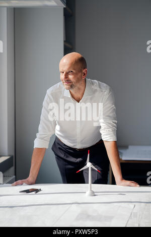 Engineer, der in seinem Büro mit Modell einer Windrad auf seinem Schreibtisch Stockfoto