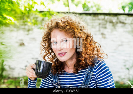 Deutschland, Köln, Porträt der Sommersprossige junge Frau mit Tasse Kaffee Stockfoto
