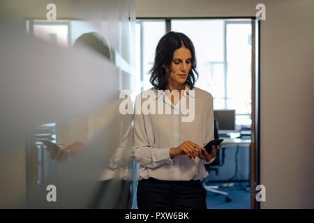 Im Büro Lesen von Nachrichten auf Ihrem Smartphone Geschäftsfrau Stockfoto