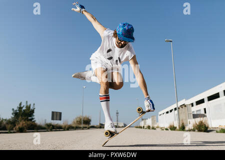 Mann in stilvollen sportlichen Outfit stehen auf Skateboard gegen den blauen Himmel Stockfoto