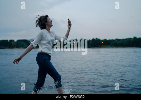 Lachende Frau am Flußufer läuft, Sie ihr Smartphone Stockfoto