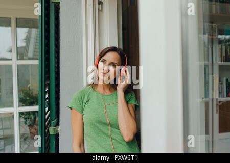 Reife Frau stehend an Terrasse Tür Hören von Musik über Kopfhörer Stockfoto