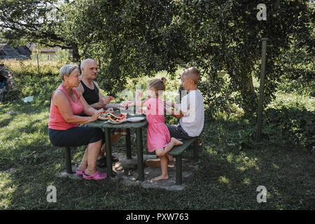 Großeltern verbringen Zeit zusammen mit Enkel und Enkelin im Garten essen Wassermelone Stockfoto