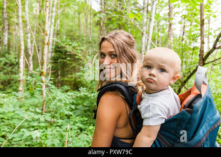 Portrait von lächelnden Mutter Wandern in den Wäldern mit Baby boy in Rucksack Stockfoto