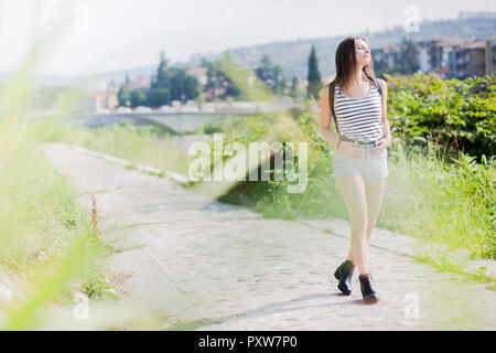 Lächelnde junge Frau zu Fuß auf einem ländlichen Weg im Sommer Stockfoto