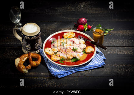 Weißwurst Salat mit gerösteten Brezel Brötchen, süßem Senf, Brezeln, rote Radieschen und Bierkrug Stockfoto