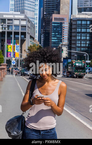 Deutschland, Frankfurt, lächelnden jungen Frau mit lockigem Haar mit Handy Stockfoto