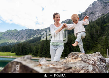 Deutschland, Bayern, Oberstdorf, Mutter helfen kleine Tochter Balancieren auf einem Baumstamm Stockfoto
