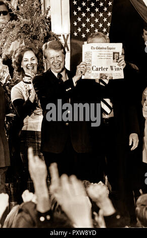 Präsidenten Jimmy Carter hält eine Zeitung mit der Schlagzeile 'Carter gewinnt!' wie er feiert mit Menschenmassen füllen die Straßen des kleinen Ebenen, Georgien in der Wahlnacht 1976. Stockfoto