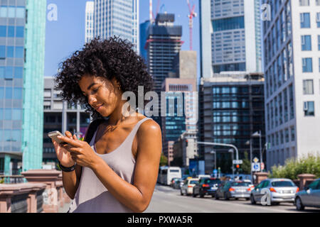 Deutschland, Frankfurt, junge Frau mit dem lockigen Haar mit Handy Stockfoto