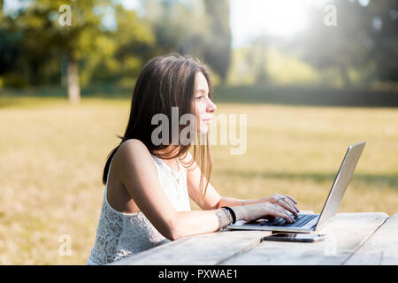 Junge Frau mit Laptop auf hölzernen Tisch im Freien Stockfoto