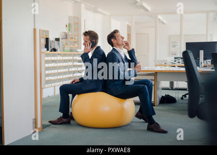 Zwei Unternehmer prüfen Smartphone mit gelben Fitness Ball im Vordergrund. Stockfoto