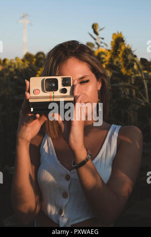 Junge Frau in einem Feld mit Sonnenblumen Bilder aufnehmen mit einem Instant Kamera Stockfoto