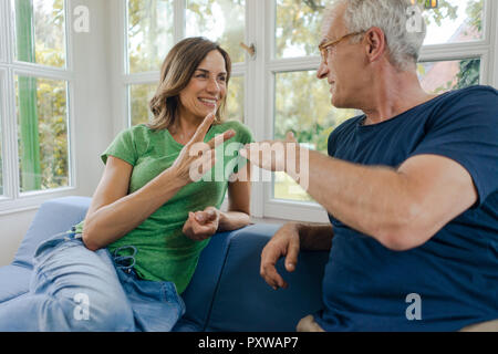 Gerne reifes Paar sitzt auf der Couch zu Hause spielt, Schere Papier Stein Stockfoto