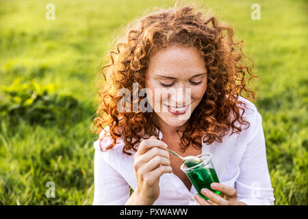 Portrait von lächelnden jungen Frau gelee Essen auf Wiese Stockfoto