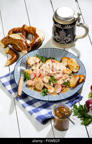 Weißwurst Salat mit gerösteten Brezel Brötchen, süßem Senf, Brezeln, rote Radieschen und Bierkrug Stockfoto