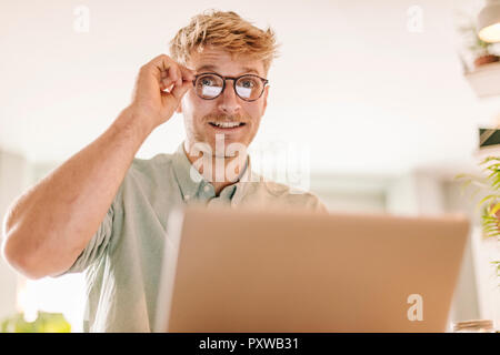 Junger Mann mit Laptop. Durch seine Brille Stockfoto