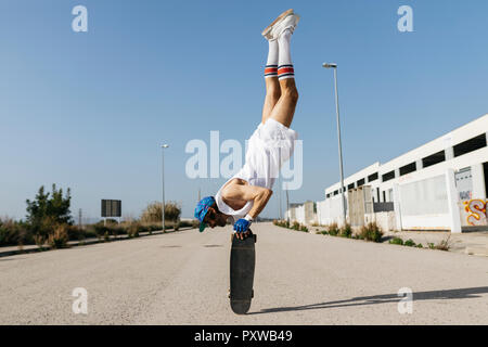 Mann in stilvollen sportlichen Outfit stehen auf Skateboard auf den Kopf Stockfoto