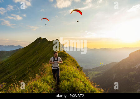 Deutschland, Bayern, Oberstdorf, Mann auf eine Wanderung in die Berge bei Sonnenuntergang mit Gleitschirm im Hintergrund Stockfoto