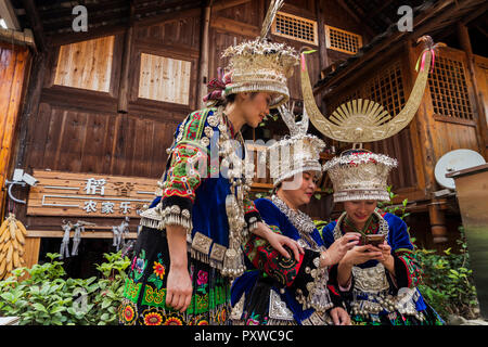 China, Yunnan, drei Miao Frauen in traditionellen Gewändern und Kopfbedeckungen mit Handy Stockfoto