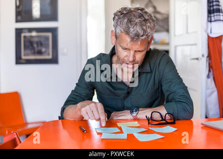 Reifer mann am Tisch zu hause sitzen auf der Suche nach Notizblöcke. Stockfoto